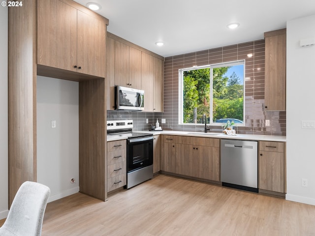 kitchen with light wood-type flooring, sink, appliances with stainless steel finishes, and decorative backsplash