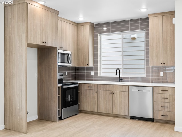 kitchen featuring light wood-type flooring, stainless steel appliances, sink, light brown cabinets, and tasteful backsplash