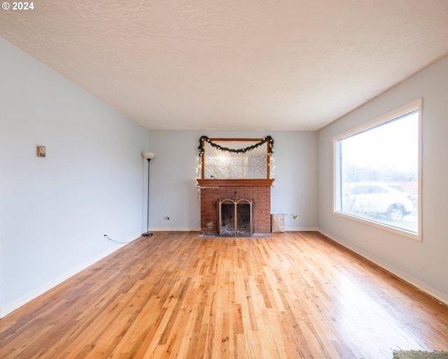 unfurnished living room with a brick fireplace, a textured ceiling, and light wood-type flooring