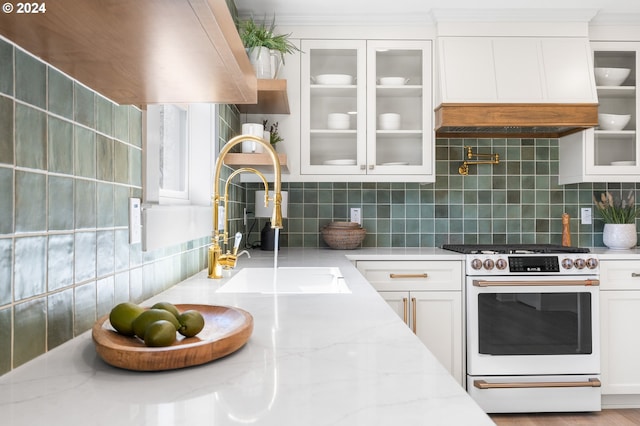 kitchen with white cabinets, backsplash, light stone counters, and high end range