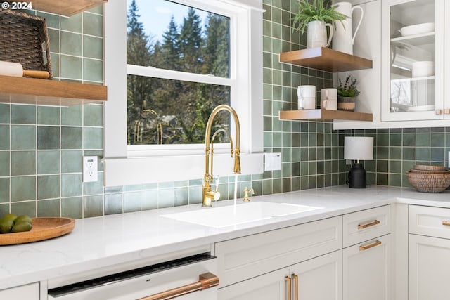 kitchen with backsplash, light stone counters, white cabinetry, and dishwasher