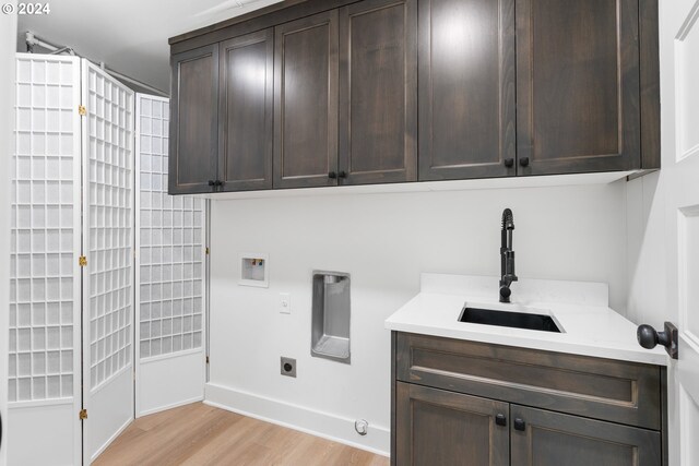 clothes washing area with electric dryer hookup, light hardwood / wood-style floors, sink, cabinets, and gas dryer hookup