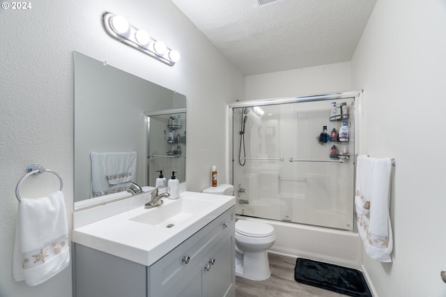 full bathroom with a textured ceiling, vanity, shower / bath combination with glass door, wood-type flooring, and toilet