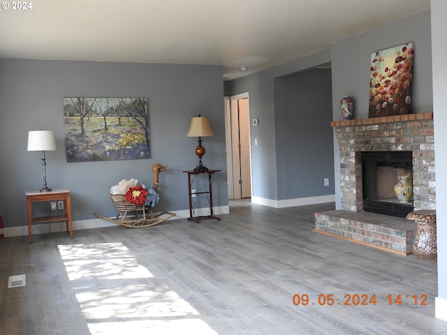 unfurnished living room with wood-type flooring and a brick fireplace