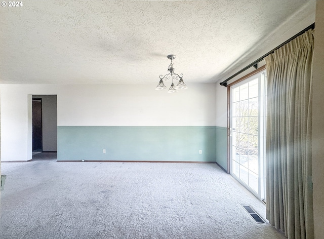 spare room featuring a textured ceiling, a notable chandelier, and light carpet