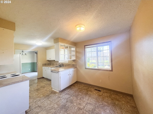 kitchen with a textured ceiling, white dishwasher, white cabinetry, and sink