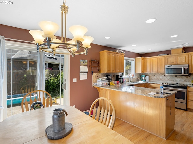 kitchen featuring decorative light fixtures, light stone countertops, appliances with stainless steel finishes, a notable chandelier, and kitchen peninsula