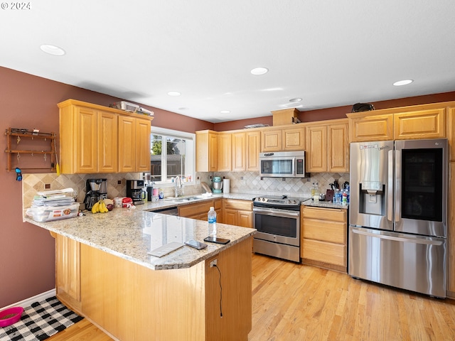 kitchen with kitchen peninsula, appliances with stainless steel finishes, light hardwood / wood-style flooring, and light stone countertops