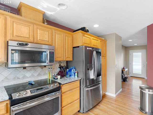 kitchen with light stone countertops, stainless steel appliances, light hardwood / wood-style flooring, and tasteful backsplash