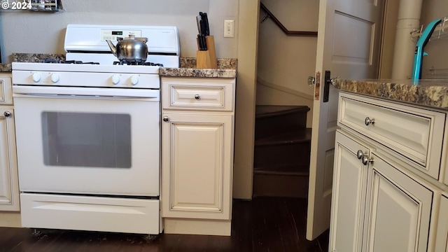 kitchen with white range with gas cooktop, dark wood-type flooring, and dark stone countertops