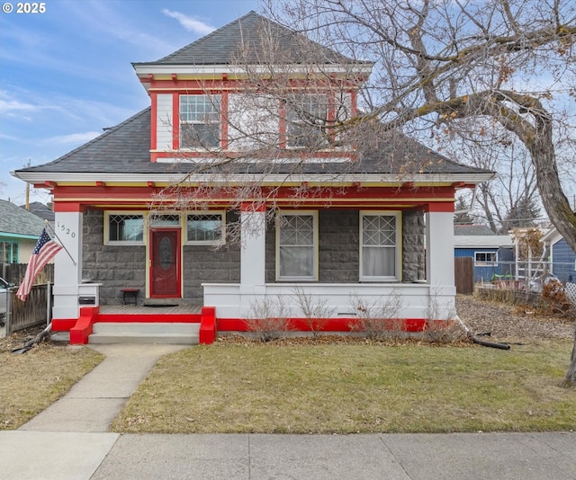 view of front of house featuring a front lawn, stone siding, a porch, fence, and roof with shingles