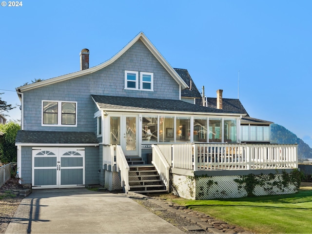 view of front of house featuring a sunroom, a garage, a front lawn, and a wooden deck