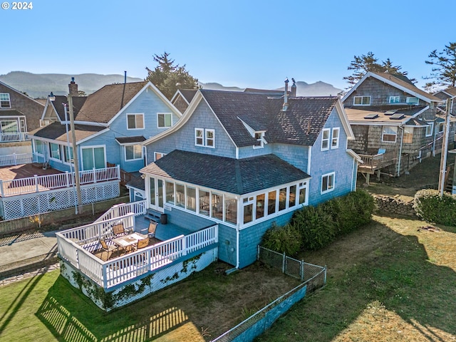 back of house featuring a deck with mountain view, a lawn, and a sunroom