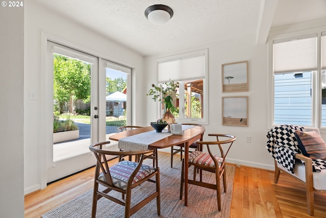 dining area featuring light wood-type flooring, french doors, and a textured ceiling