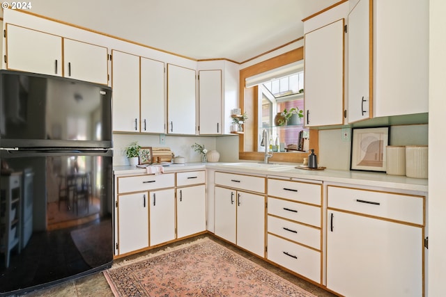 kitchen featuring white cabinets, black refrigerator, and sink