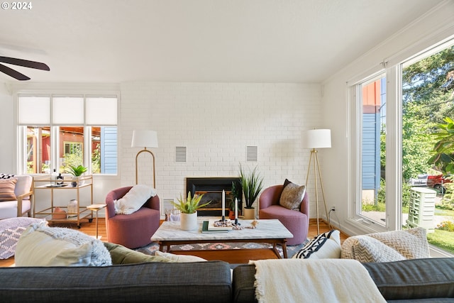 living room featuring a brick fireplace, plenty of natural light, wood-type flooring, and brick wall