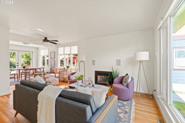 living room with a brick fireplace, light hardwood / wood-style flooring, brick wall, and ceiling fan