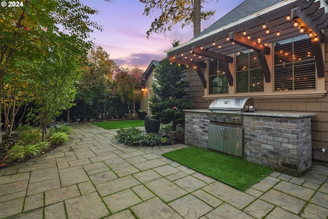 patio terrace at dusk with an outdoor kitchen, a grill, and a pergola