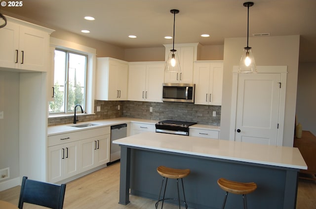 kitchen featuring a center island, sink, stainless steel appliances, decorative light fixtures, and white cabinets