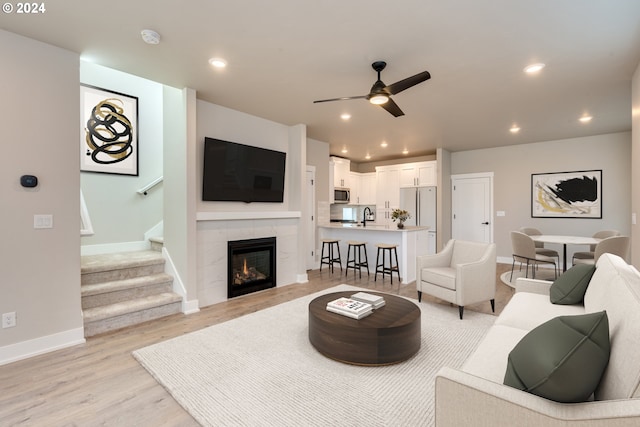 living room with a fireplace, ceiling fan, light hardwood / wood-style flooring, and sink