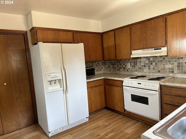 kitchen featuring tasteful backsplash, a textured ceiling, white appliances, and light wood-type flooring