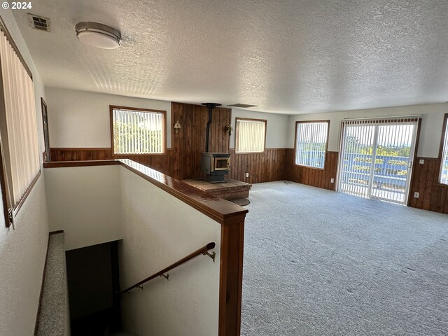 staircase featuring carpet, a healthy amount of sunlight, a wood stove, and a textured ceiling