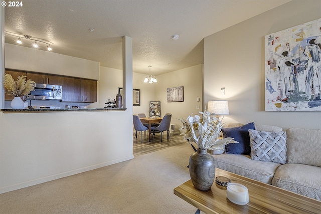 carpeted living area featuring a textured ceiling, baseboards, and an inviting chandelier