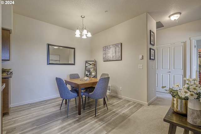 dining room with light wood finished floors, baseboards, a textured ceiling, and an inviting chandelier