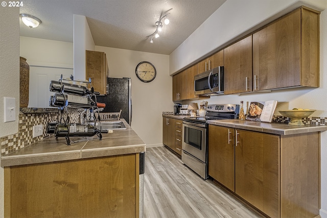 kitchen with backsplash, appliances with stainless steel finishes, light wood-style floors, and a textured ceiling