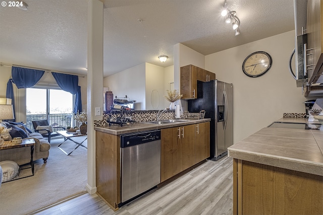 kitchen with stainless steel countertops, a sink, appliances with stainless steel finishes, a textured ceiling, and light wood-style flooring