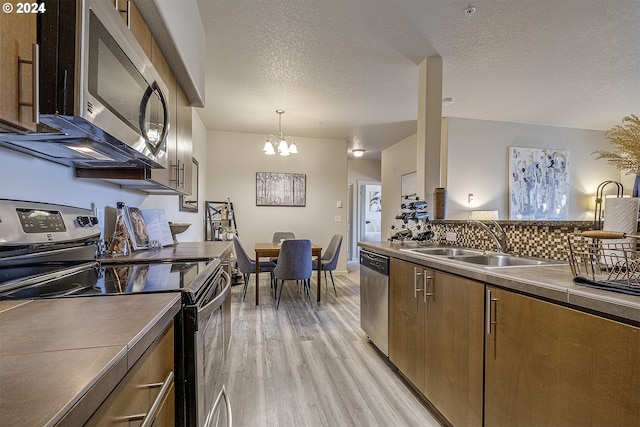 kitchen with a notable chandelier, a sink, light wood finished floors, appliances with stainless steel finishes, and brown cabinets