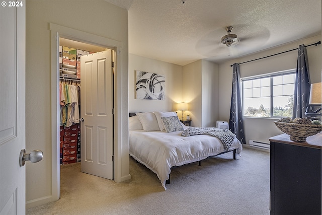 bedroom with a baseboard radiator, a spacious closet, light colored carpet, and a textured ceiling