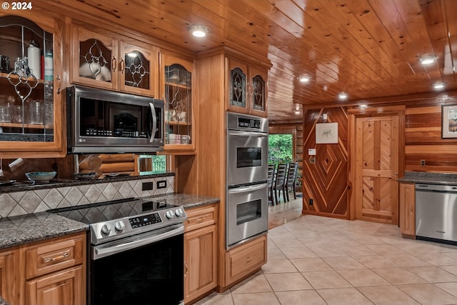 kitchen featuring wood walls, wooden ceiling, dark stone countertops, appliances with stainless steel finishes, and light tile patterned flooring