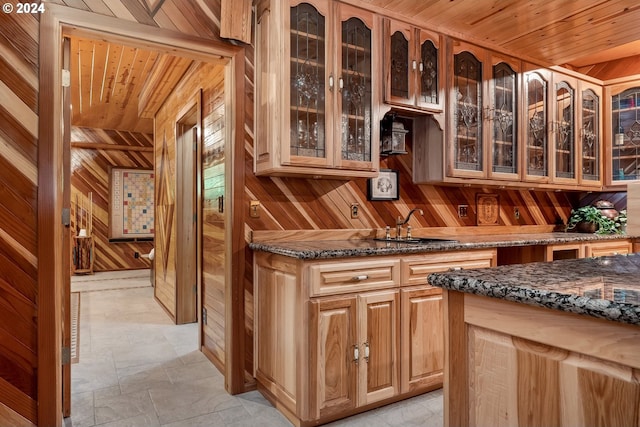 kitchen with sink, dark stone counters, wooden walls, and wood ceiling