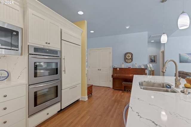 kitchen featuring white cabinets, sink, decorative light fixtures, stainless steel appliances, and light hardwood / wood-style floors