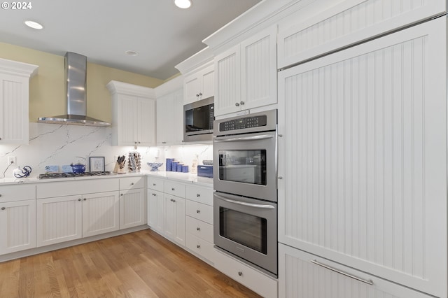 kitchen featuring white cabinets, appliances with stainless steel finishes, light wood-type flooring, and wall chimney range hood