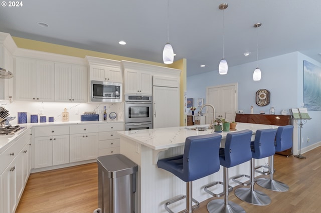 kitchen with pendant lighting, an island with sink, light hardwood / wood-style flooring, white cabinetry, and appliances with stainless steel finishes