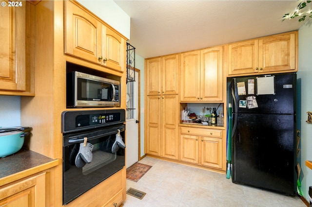 kitchen with light brown cabinetry, light tile patterned floors, black appliances, and a textured ceiling