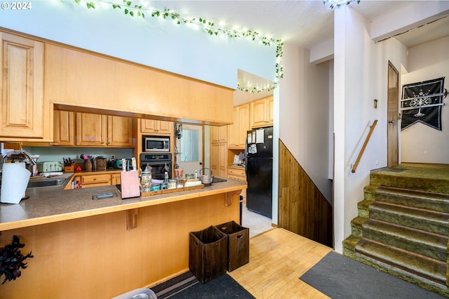 kitchen featuring black appliances, sink, light hardwood / wood-style flooring, kitchen peninsula, and a breakfast bar area