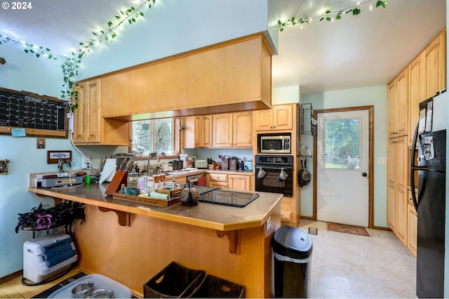 kitchen featuring light brown cabinets, rail lighting, kitchen peninsula, a kitchen bar, and black appliances