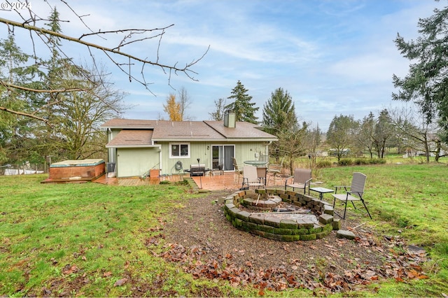 back of property with a fire pit, a patio, a lawn, and a hot tub