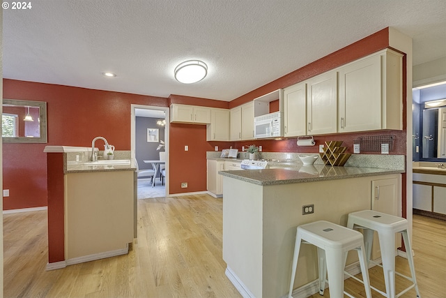 kitchen with light wood-type flooring, a textured ceiling, sink, a breakfast bar area, and an island with sink