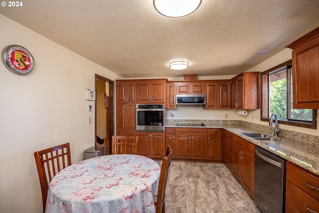 kitchen featuring a textured ceiling, stainless steel appliances, sink, light wood-type flooring, and stone counters