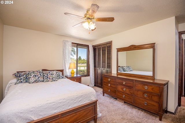 bedroom with a textured ceiling, a closet, ceiling fan, and light carpet