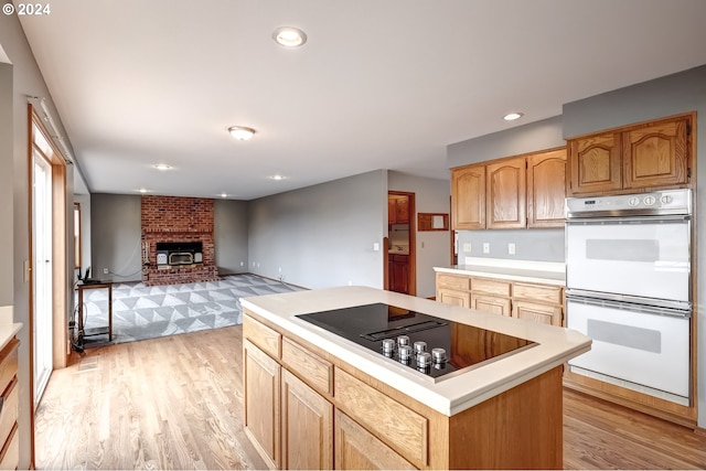 kitchen featuring double oven, a fireplace, light hardwood / wood-style flooring, and black electric cooktop