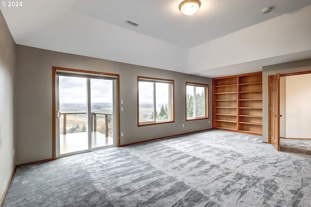 unfurnished living room featuring a raised ceiling, carpet floors, built in shelves, and plenty of natural light