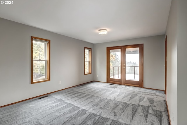 spare room featuring a healthy amount of sunlight, french doors, and light carpet