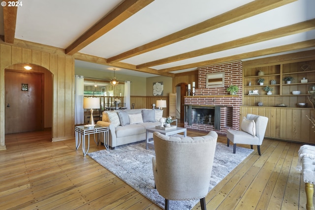 living room with wooden walls, beamed ceiling, light hardwood / wood-style floors, and a brick fireplace