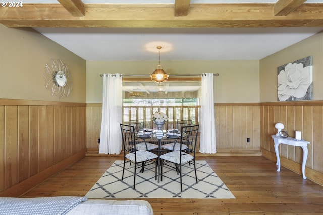 dining space with beam ceiling, hardwood / wood-style flooring, and wooden walls