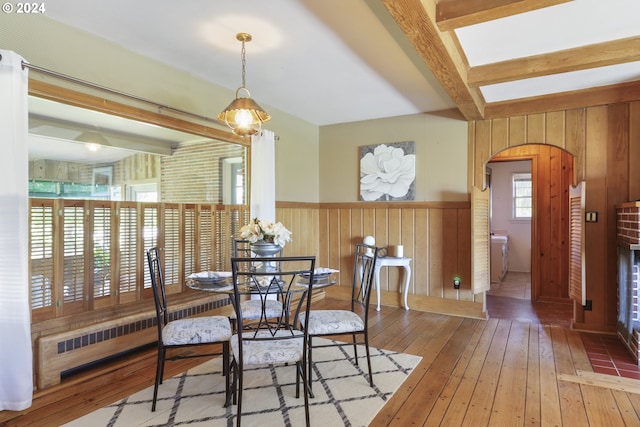 dining space featuring beamed ceiling, wood-type flooring, radiator heating unit, and wooden walls